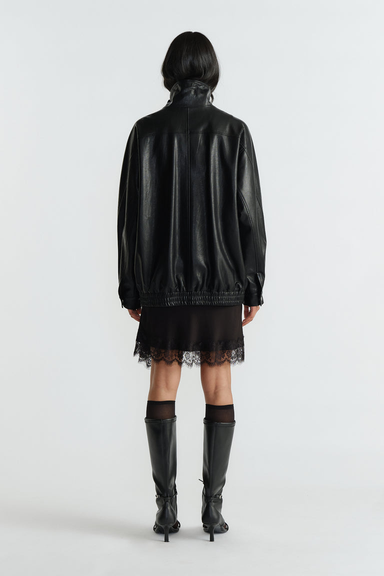 Back view of woman wearing an oversized black jacket with gathered hem paired with a lace-trimmed black dress and knee boots