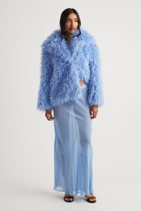 Model wearing a light blue sheer maxi skirt with a voluminous textured blue jacket and black open-toe heels