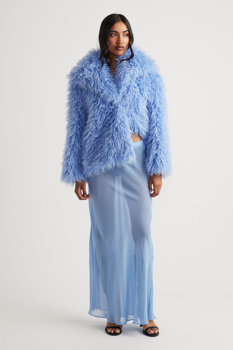 Model wearing a light blue sheer maxi skirt with a voluminous textured blue jacket and black open-toe heels