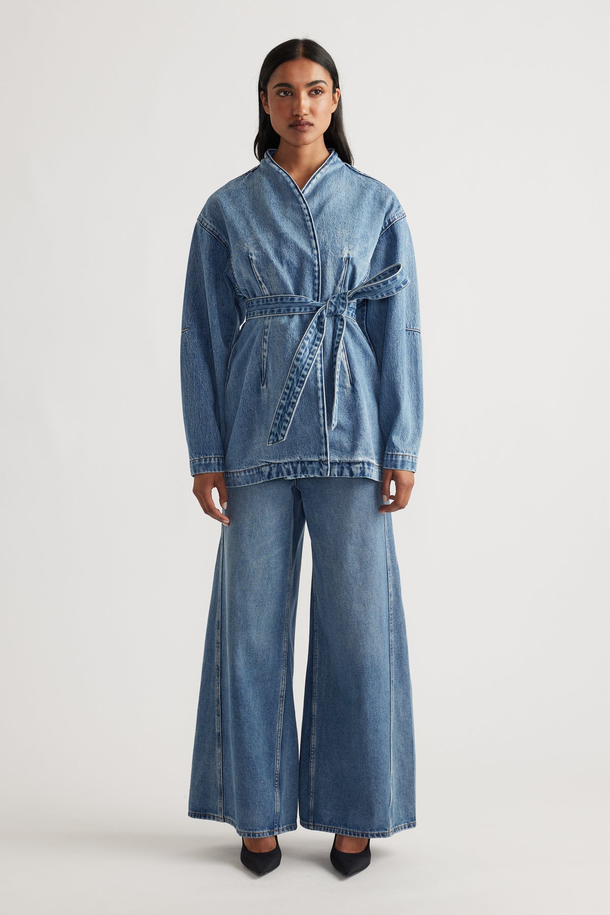Woman wearing a belted denim jacket paired with high-waisted wide leg blue jeans and black pointed shoes