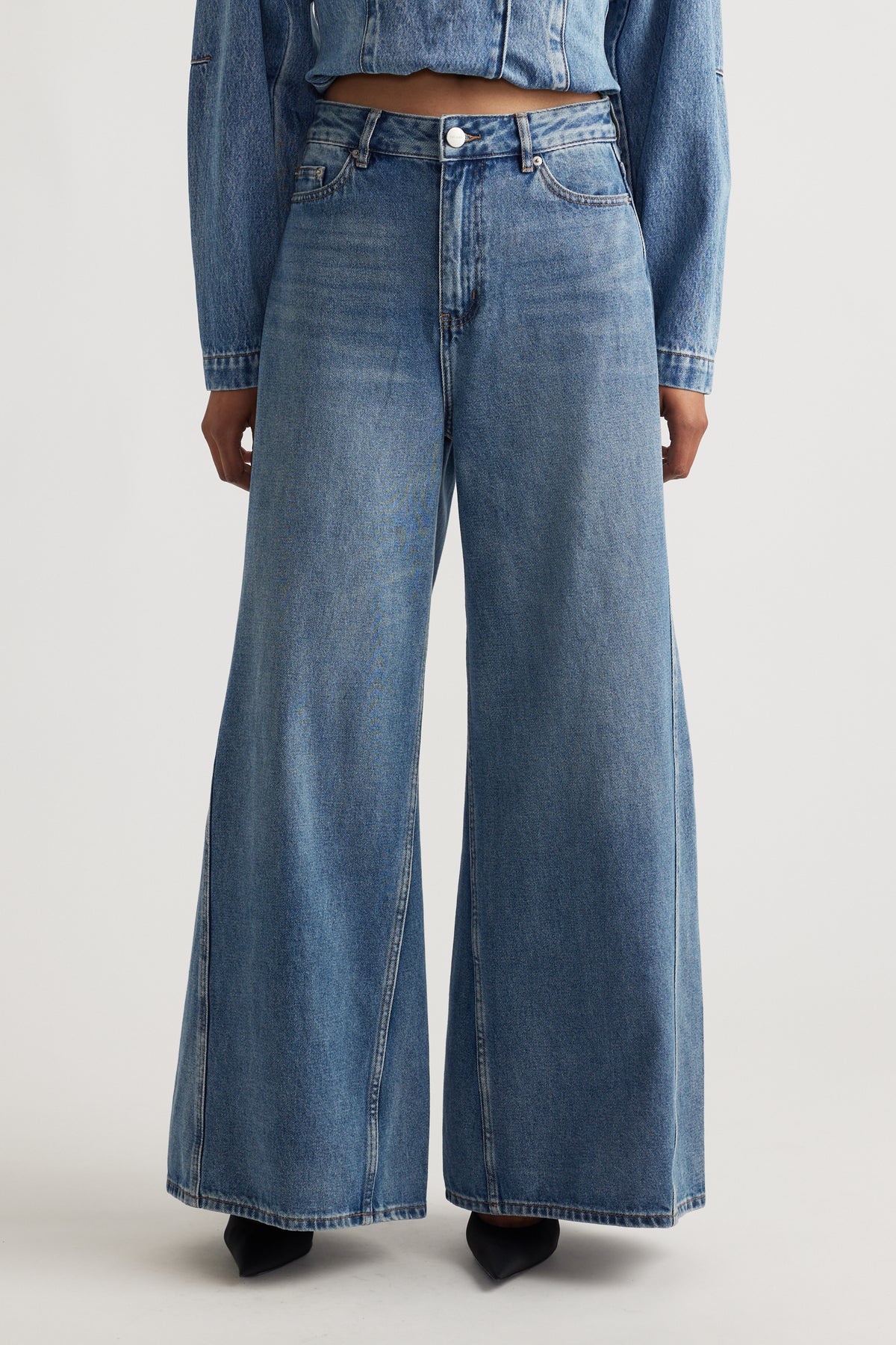 Wide leg denim jeans in a mid-blue wash, styled with a cropped denim jacket and black pointed heels.