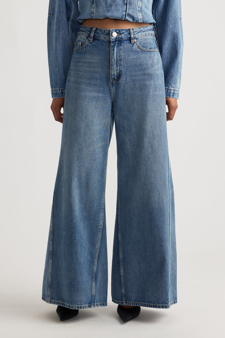 Wide leg denim jeans in a mid-blue wash, styled with a cropped denim jacket and black pointed heels.
