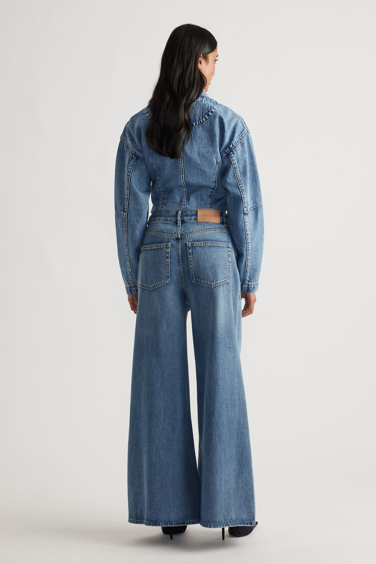 Woman wearing mid-blue wide-leg jeans with high waist and matching cropped denim jacket, viewed from behind