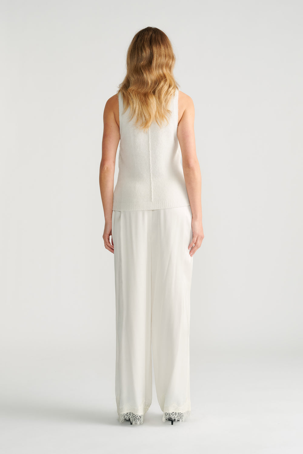 Woman seen from behind wearing a textured ivory knit tank paired with loose, flowing wide-leg trousers in ivory.