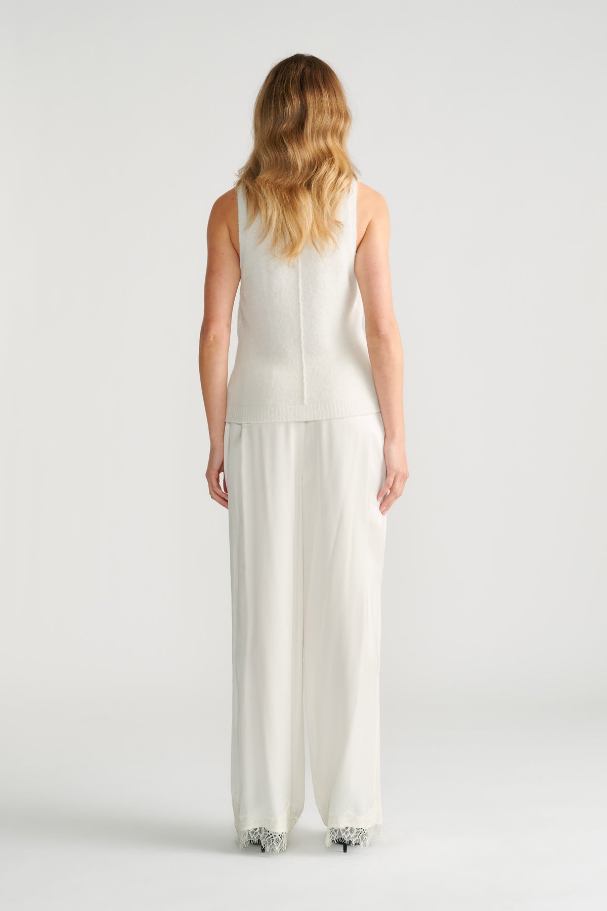 Woman seen from behind wearing a textured ivory knit tank paired with loose, flowing wide-leg trousers in ivory.