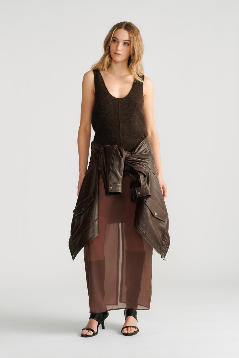 Woman wearing a dark brown fluffy knit tank with a tied leather jacket and sheer brown maxi skirt paired with black heels