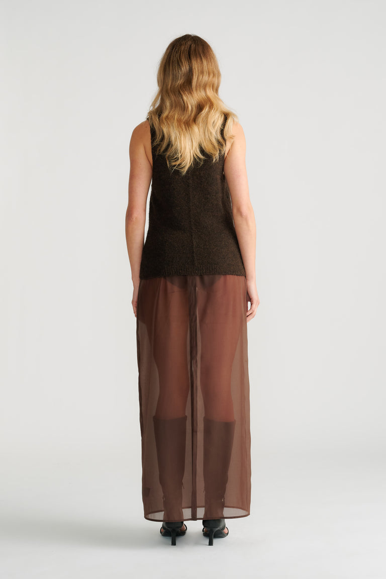 Woman wearing a soft textured brown knit tank paired with a sheer brown maxi skirt and black heels seen from behind.