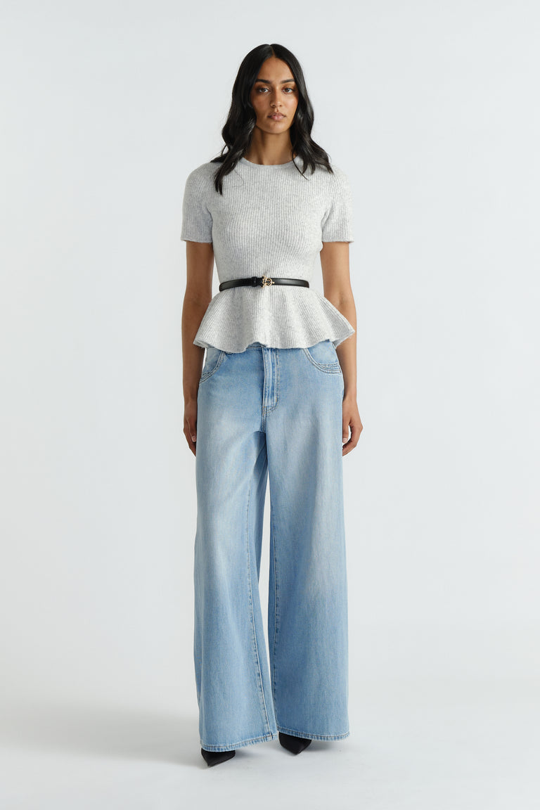 Woman wearing a light grey peplum knit top with a black belt paired with wide-leg light blue denim jeans and black heels