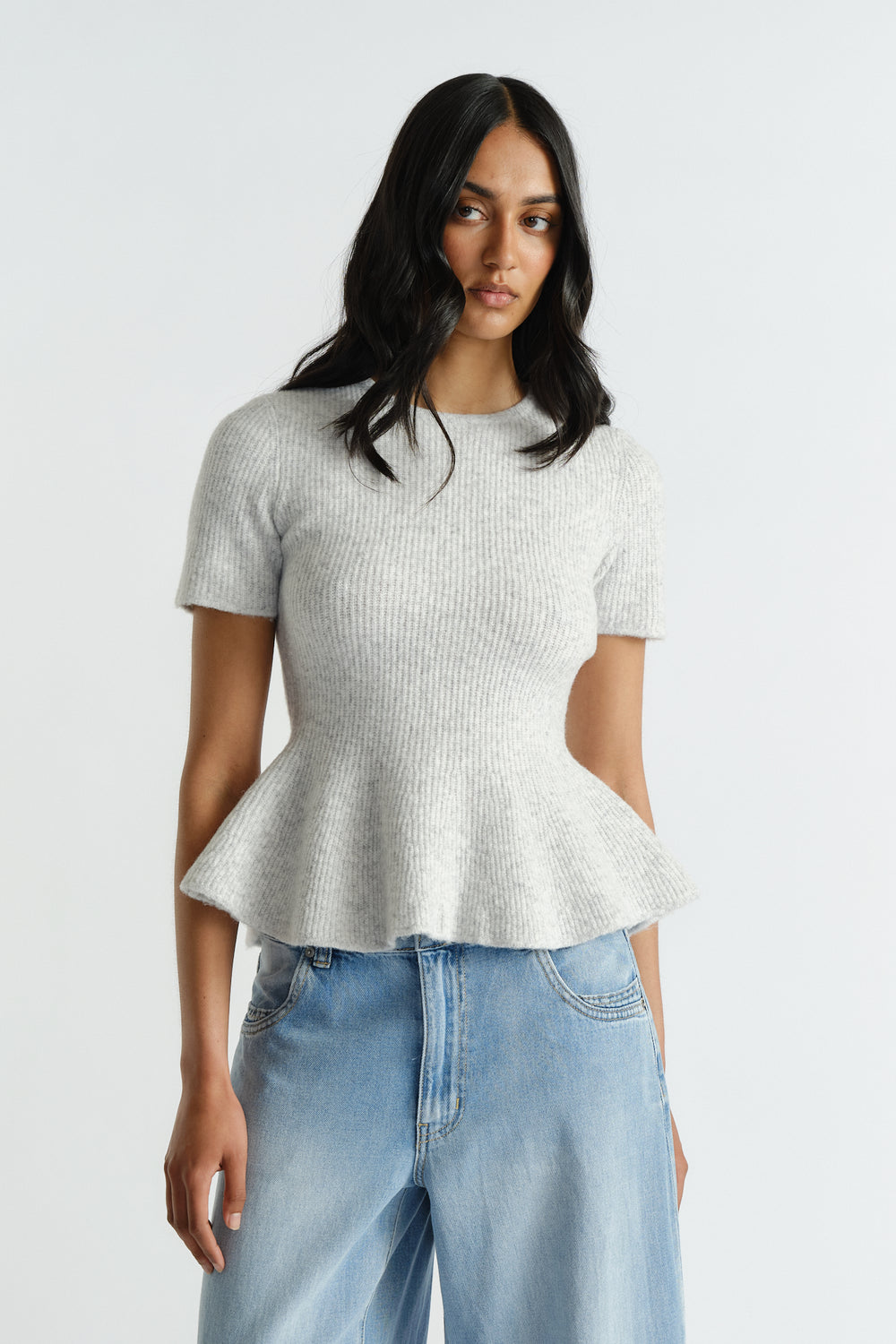Woman wearing a light grey short sleeve knit top with a flared peplum hem paired with relaxed light wash jeans