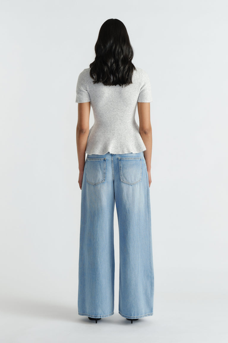Woman wearing a light grey peplum knit top paired with wide-leg light blue denim jeans for a casual look
