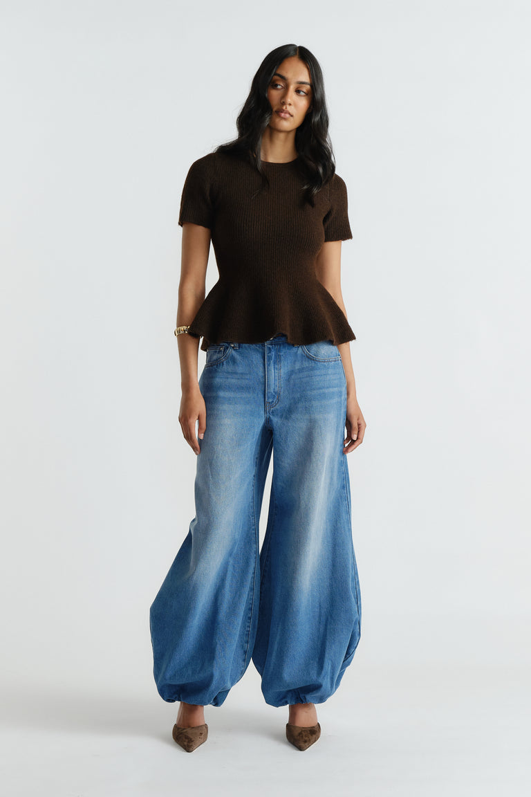 Woman wearing a rich mocha peplum knit tee paired with wide-leg light blue denim jeans and pointed toe heels