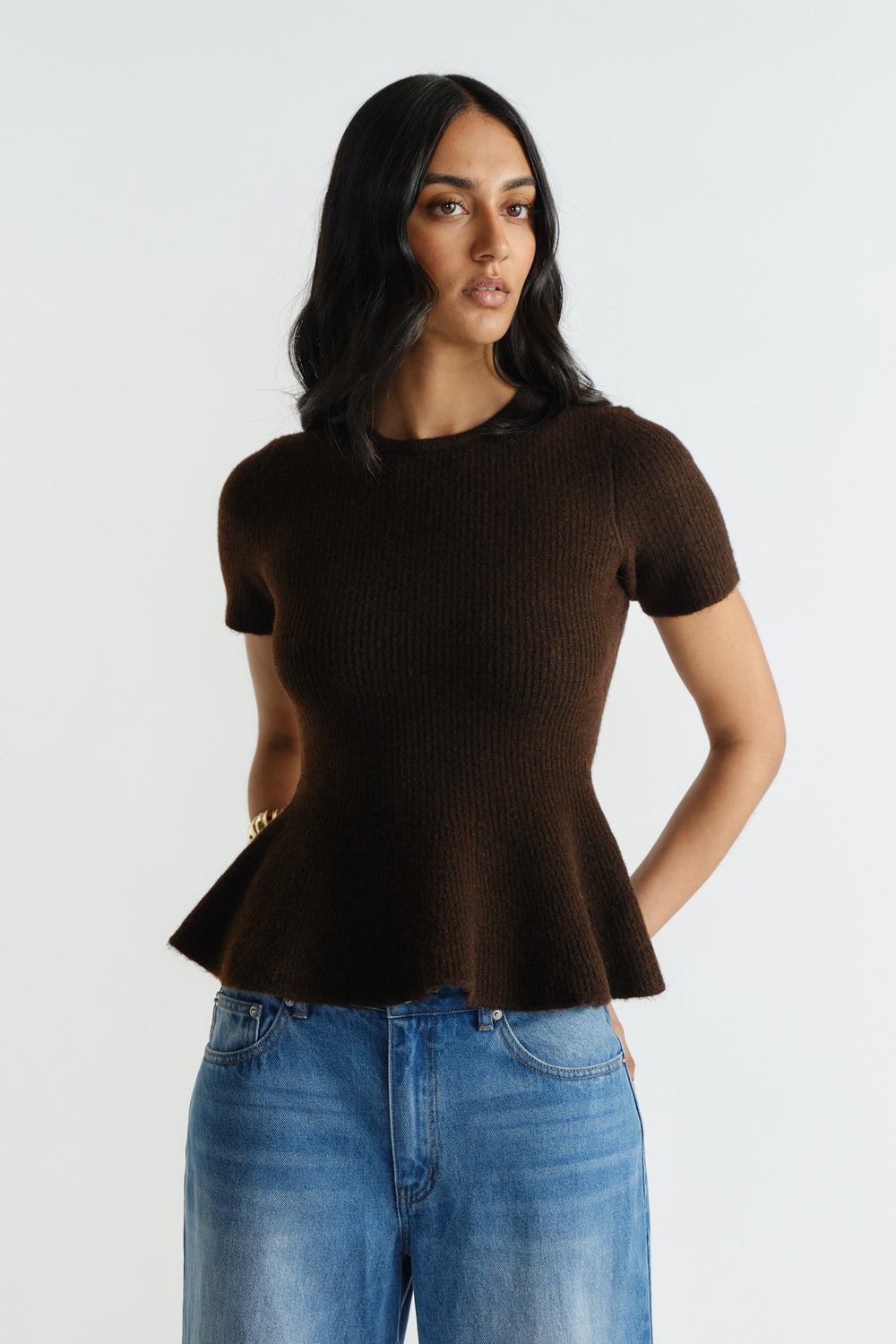 Woman wearing a rich mocha short-sleeve knit top with a peplum hem paired with relaxed fit blue denim jeans