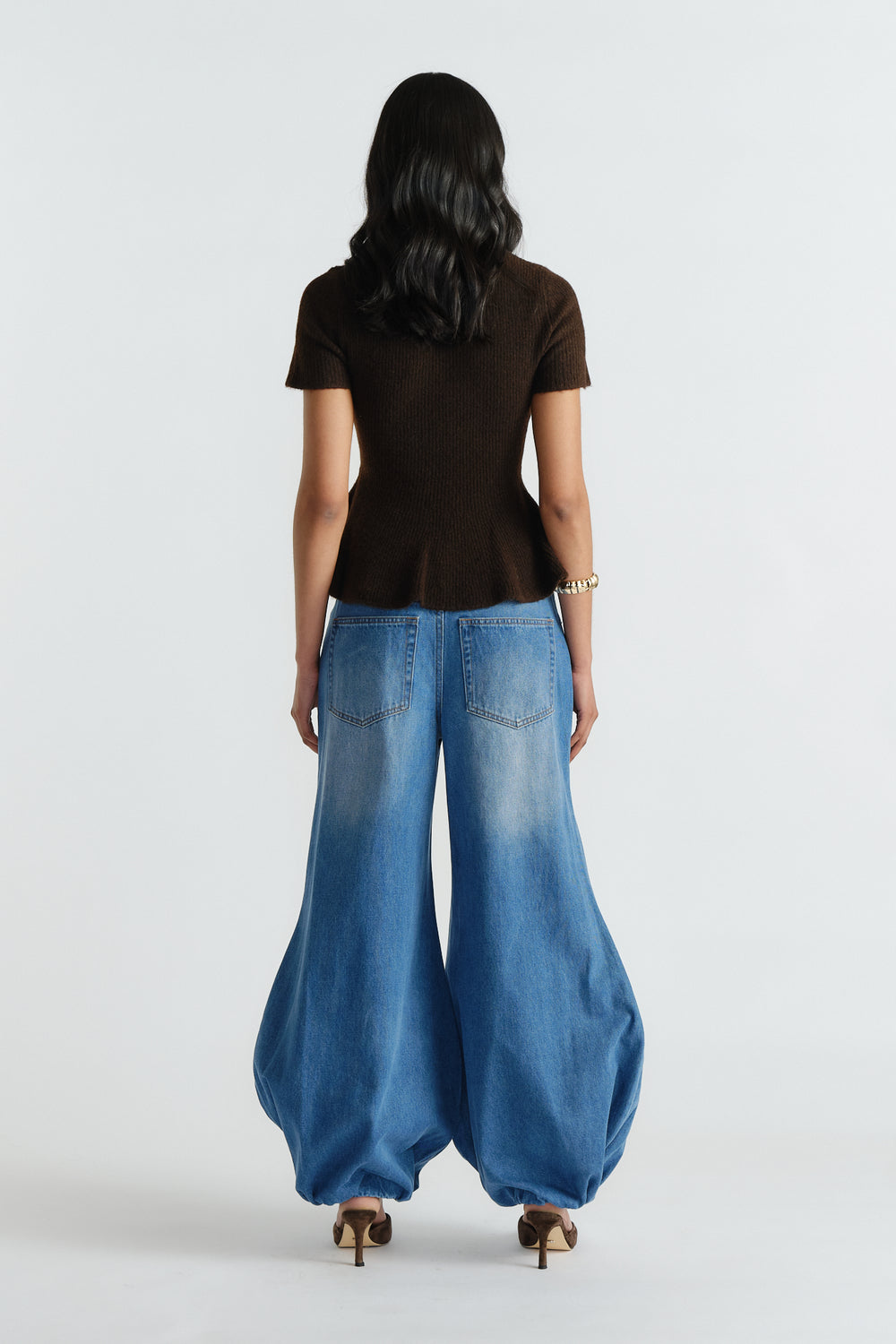 Woman wearing a fitted brown peplum knit top paired with wide-leg light blue denim jeans and heels, back view