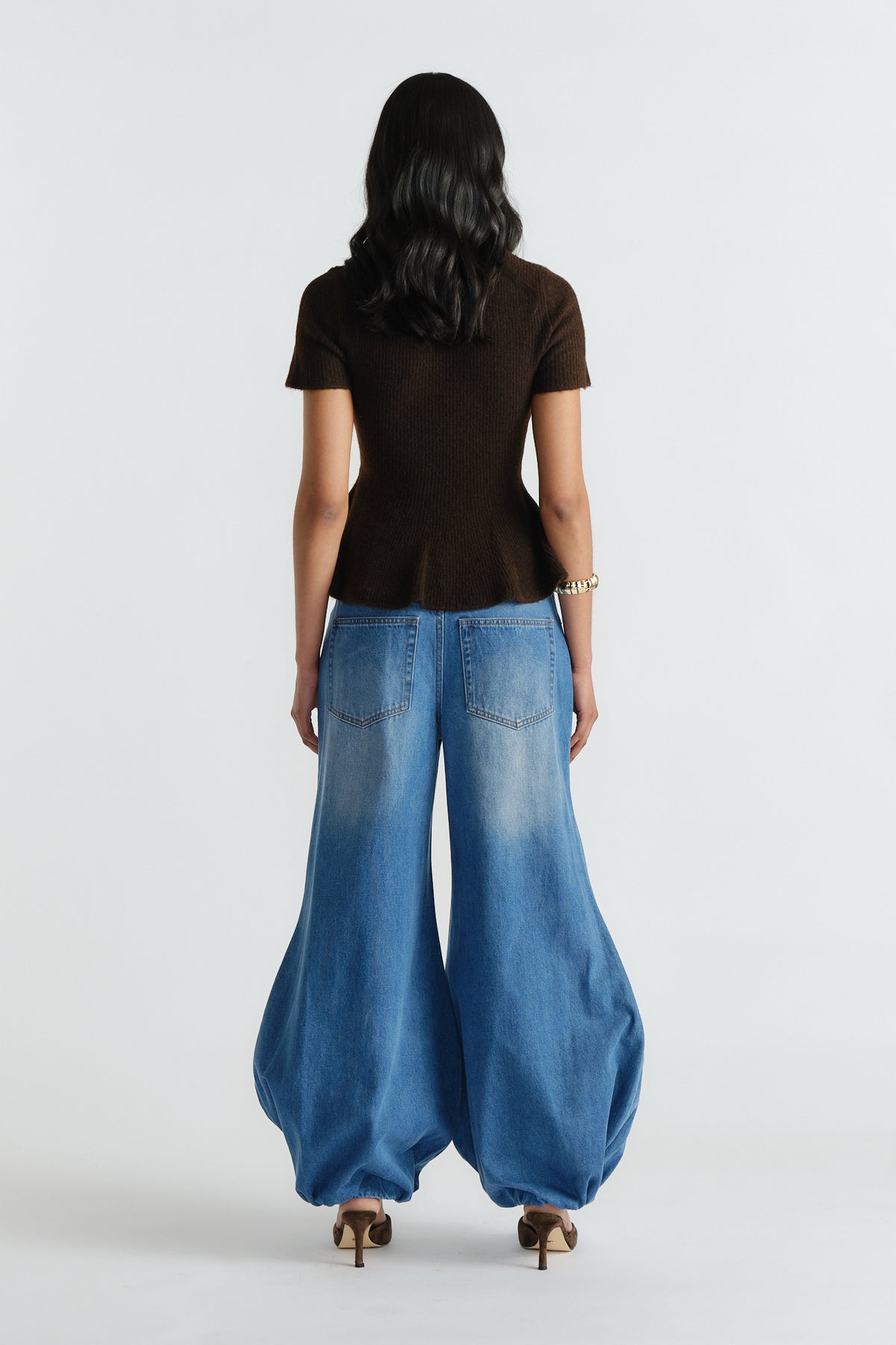Woman wearing a fitted brown peplum knit top paired with wide-leg light blue denim jeans and heels, back view