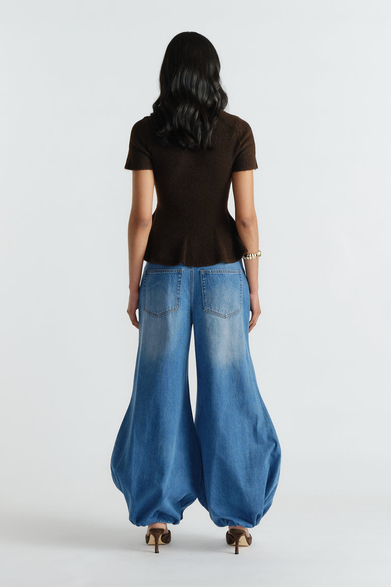 Woman wearing a fitted brown peplum knit top paired with wide-leg light blue denim jeans and heels, back view