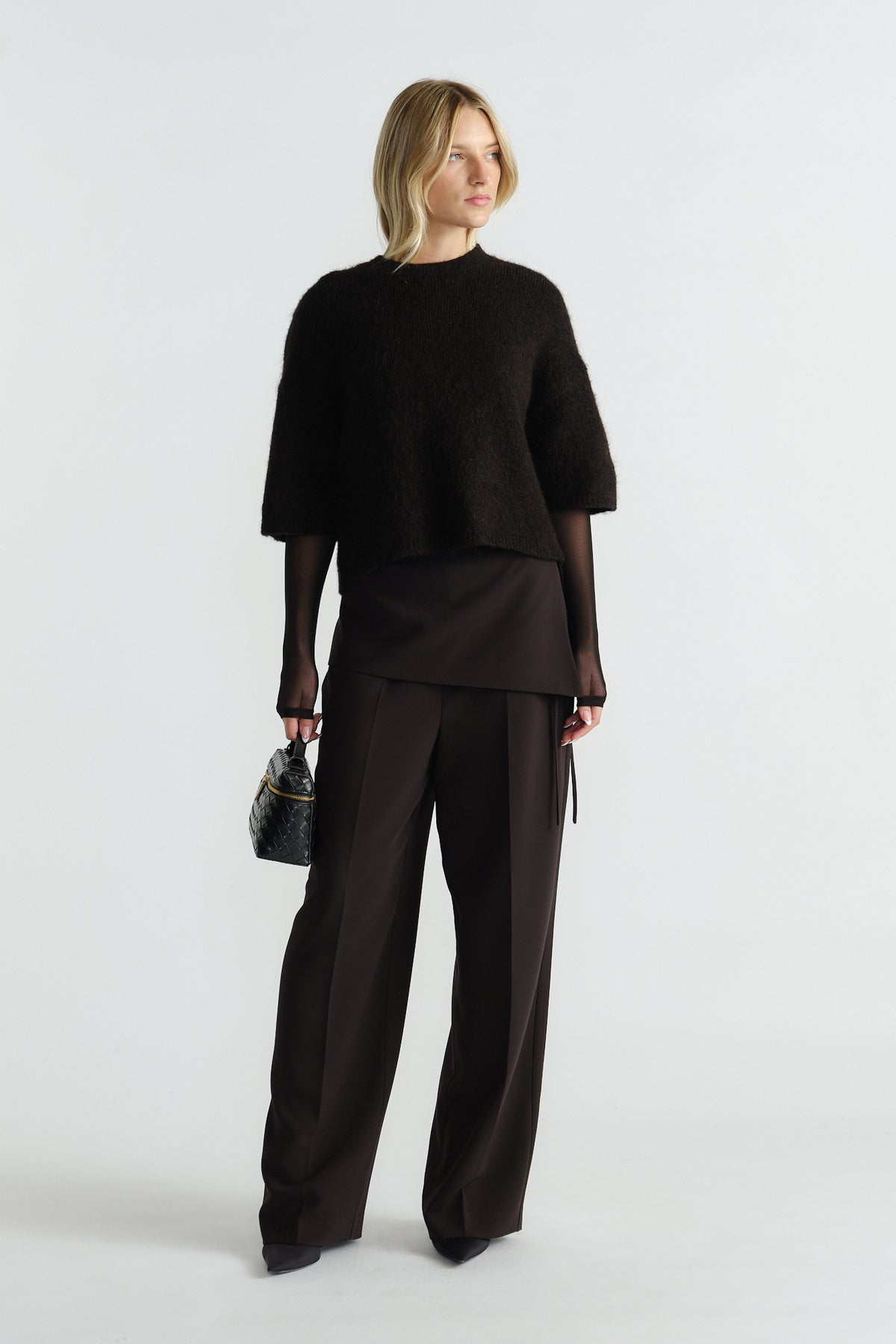 Woman wearing a black fluffy knit tee layered over a sheer long-sleeve top with wide-leg tailored black pants.