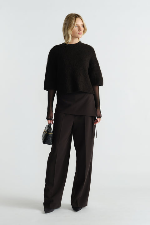 Woman wearing a black fluffy knit tee layered over a sheer long-sleeve top with wide-leg tailored black pants.