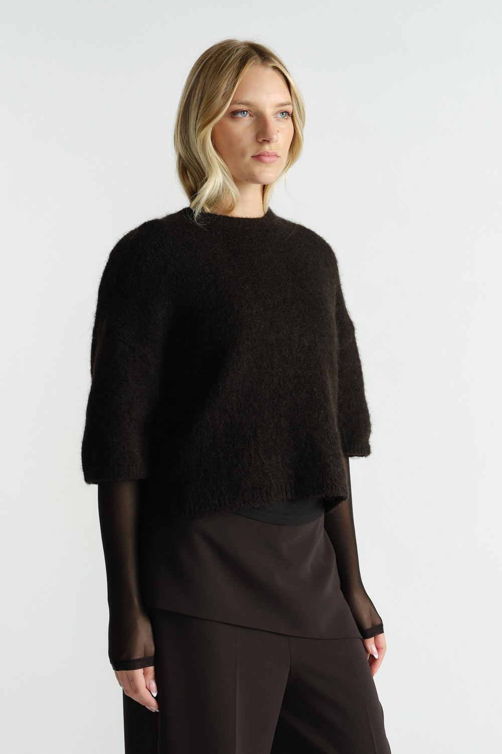 Woman wearing a black fluffy knit tee with three-quarter sleeves layered over a sheer long-sleeve top and dark pants.