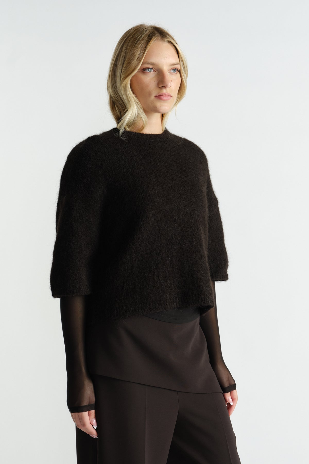 Woman wearing a black fluffy knit tee with three-quarter sleeves layered over a sheer long-sleeve top and dark pants.