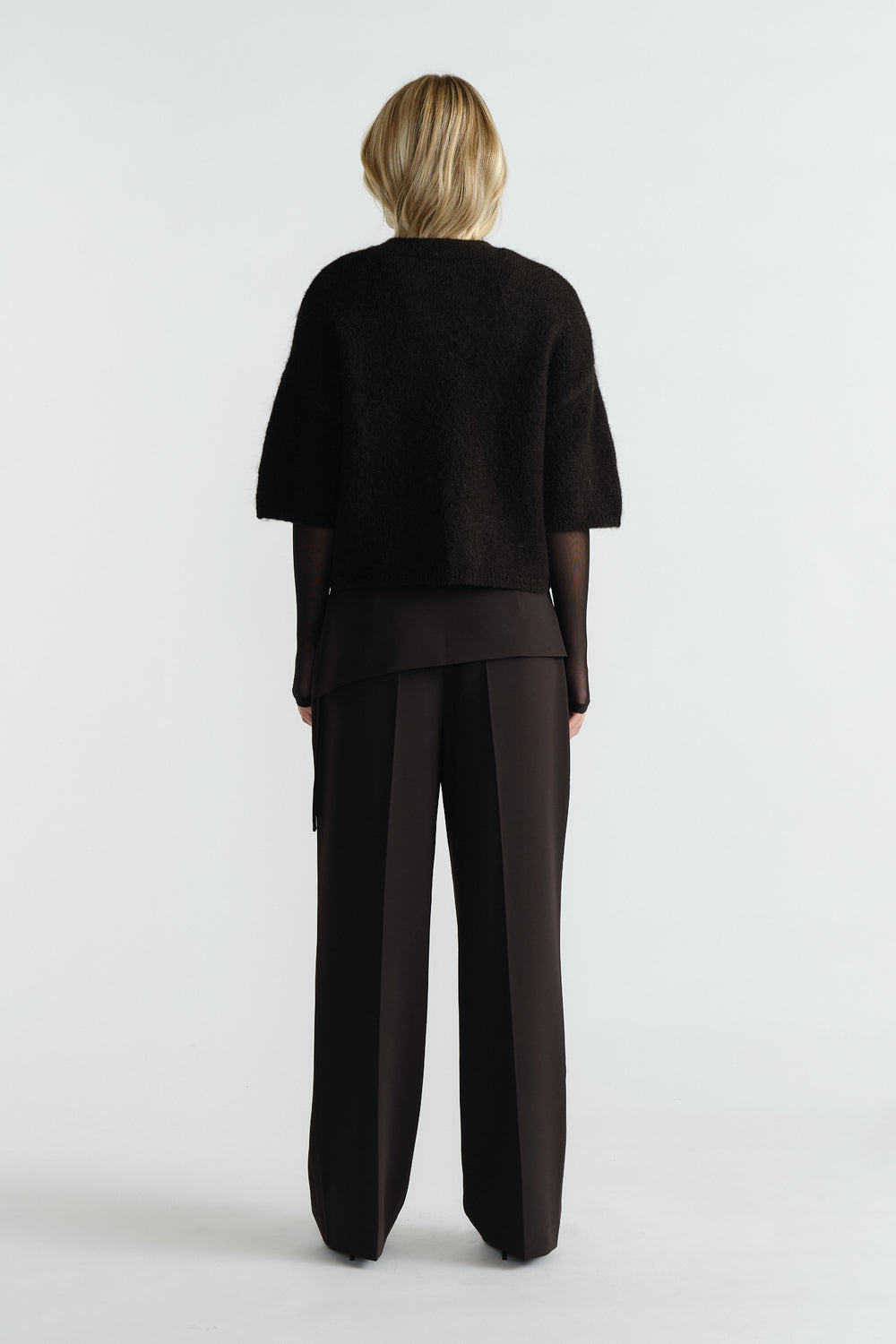 Woman wearing a black fluffy knit tee layered over a sheer long-sleeve top paired with wide-leg black pants, back view.