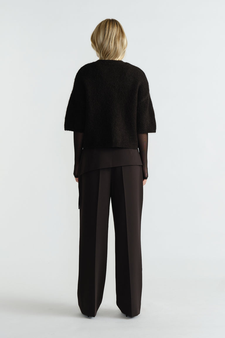 Woman wearing a black fluffy knit tee layered over a sheer long-sleeve top paired with wide-leg black pants, back view.