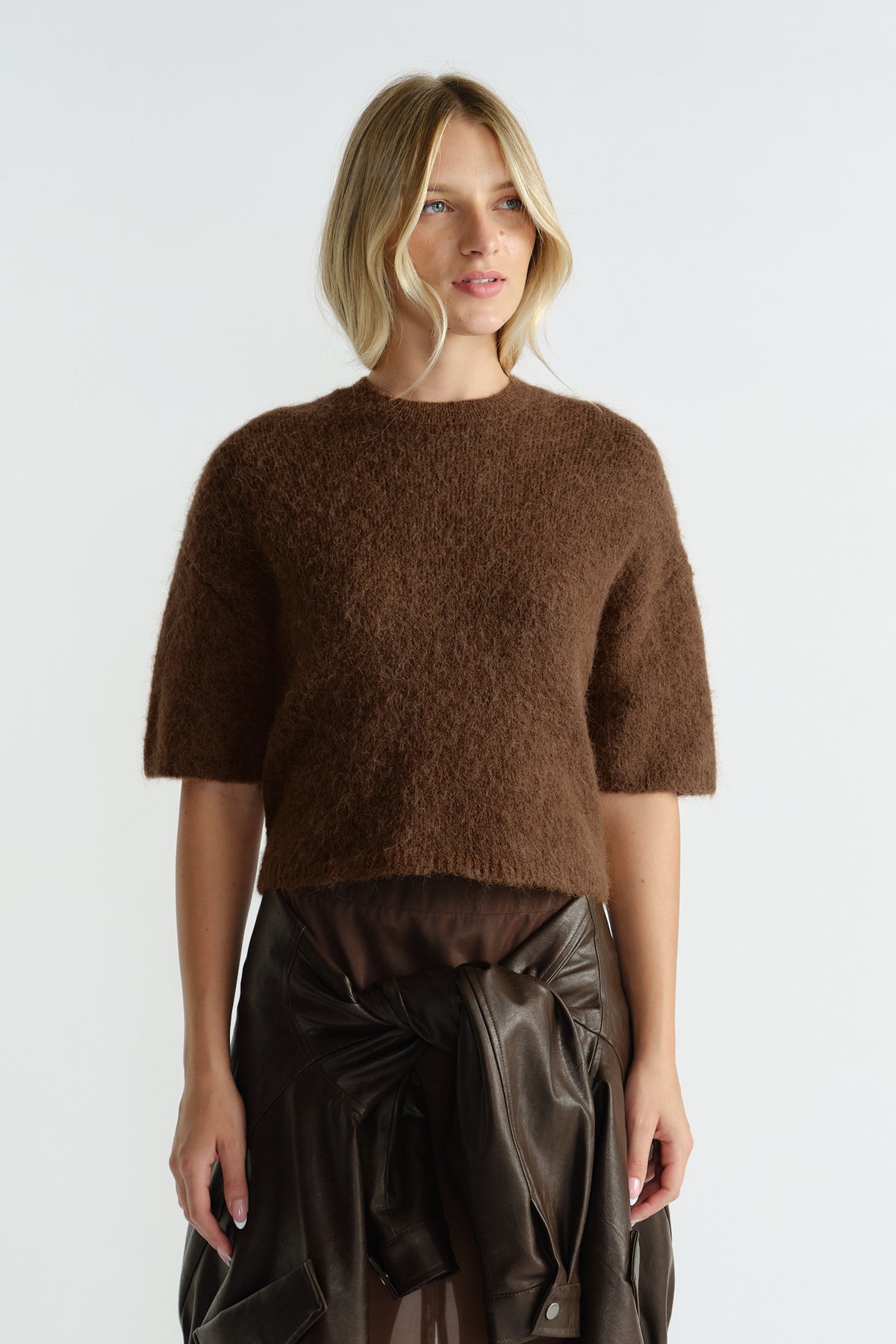 Woman wearing a rich brown fluffy knit tee with elbow-length sleeves paired with a dark leather jacket tied at the waist.