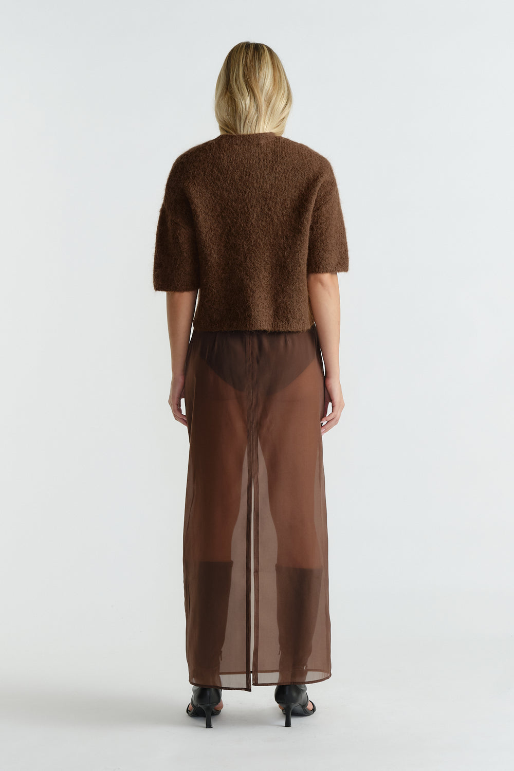 Woman wearing a caramel brown fluffy knit tee paired with a sheer brown maxi skirt and black heeled sandals.