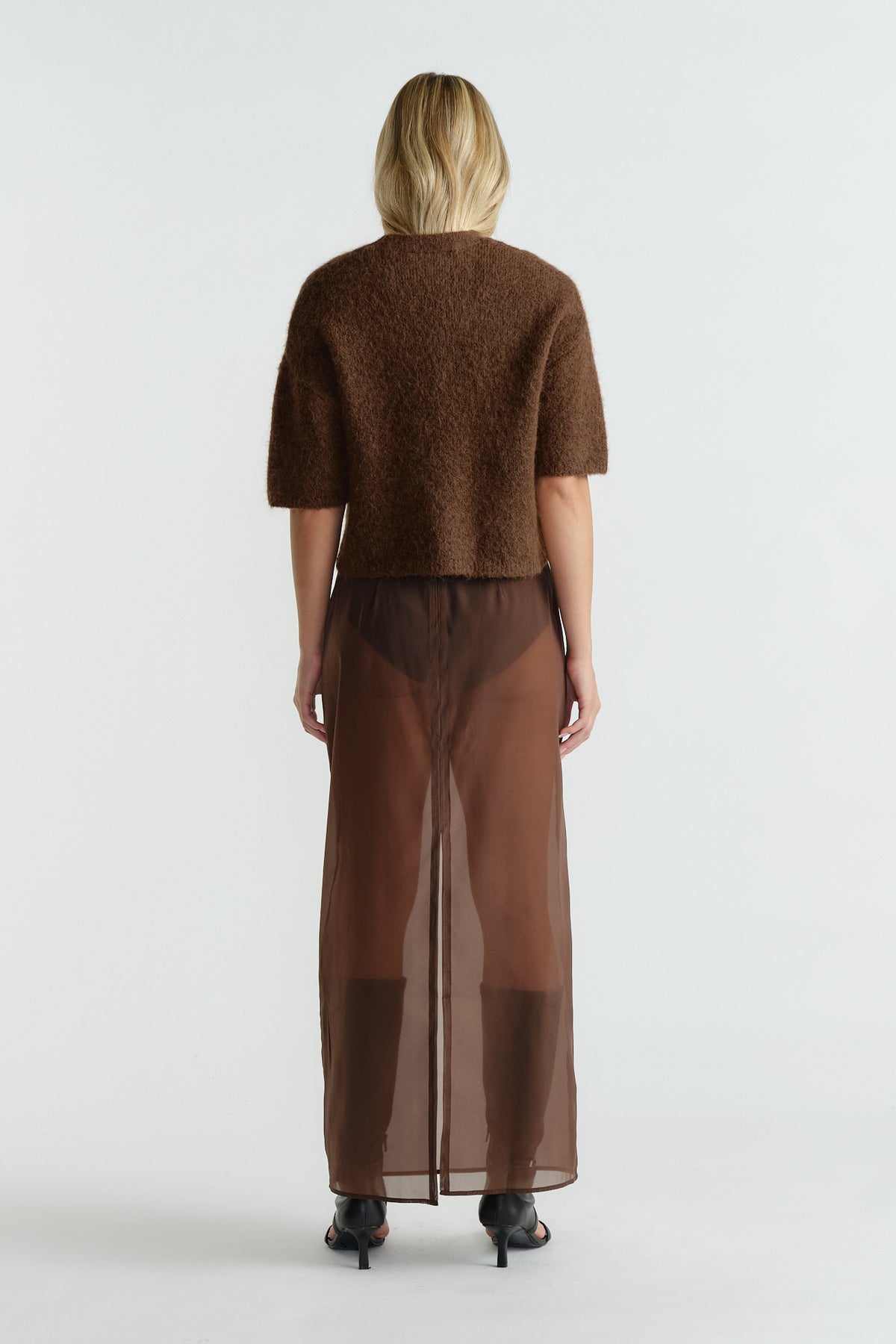 Woman wearing a caramel brown fluffy knit tee paired with a sheer brown maxi skirt and black heeled sandals.