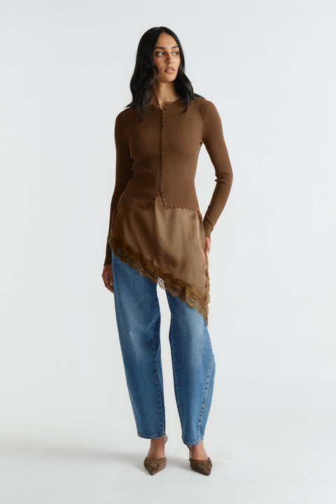Woman wearing a brown scalloped button top with lace trim paired with relaxed blue jeans and pointed shoes.