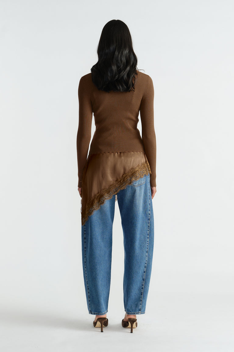 Back view of woman wearing a fitted brown knit top layered with a scalloped asymmetric caramel silk detail and relaxed blue jeans