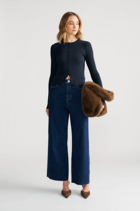 Woman wearing a navy scallop-edge button top paired with wide-leg denim jeans and holding a brown faux fur clutch.