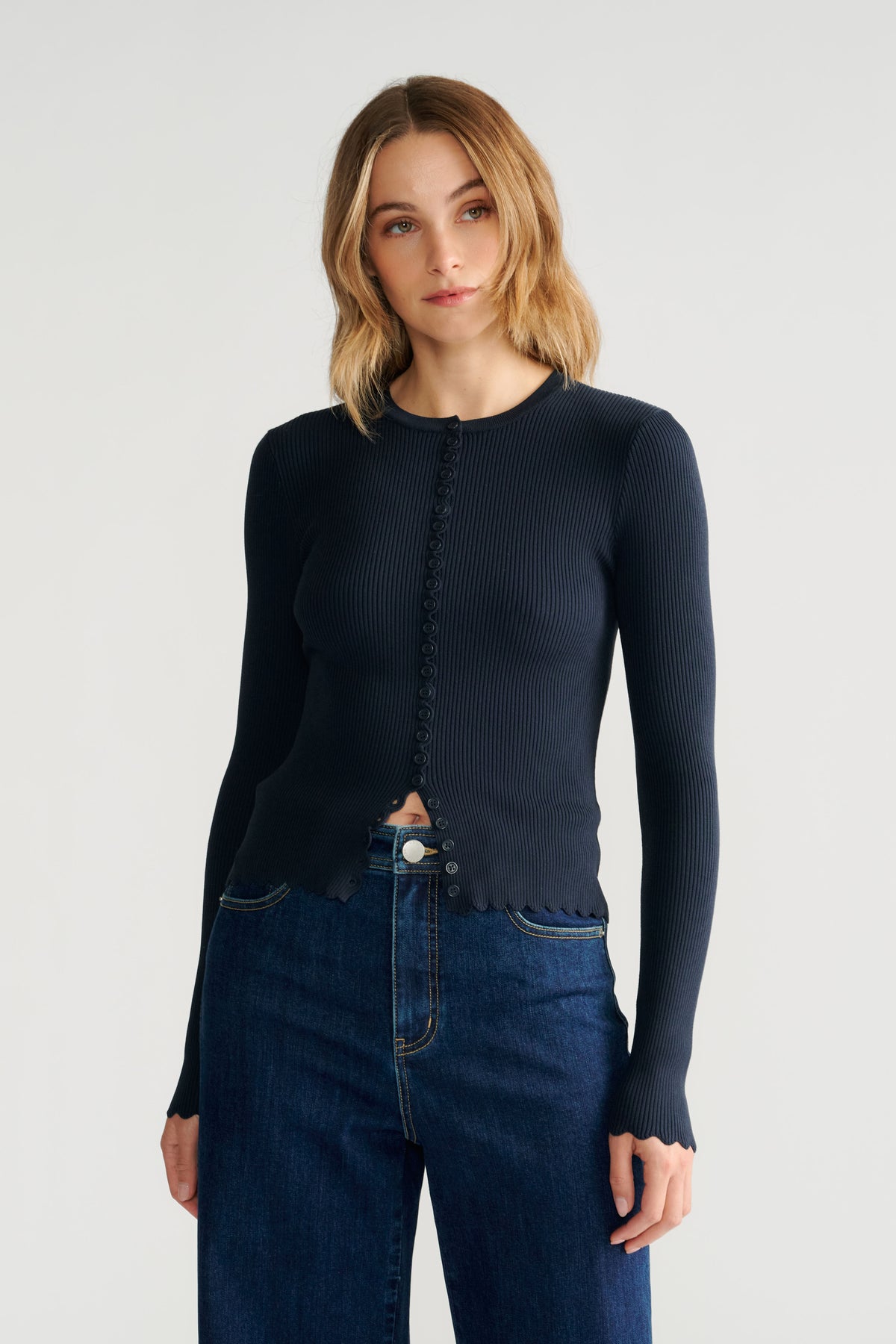 Woman wearing navy scallop-edge button-up ribbed top paired with dark blue high-waisted jeans