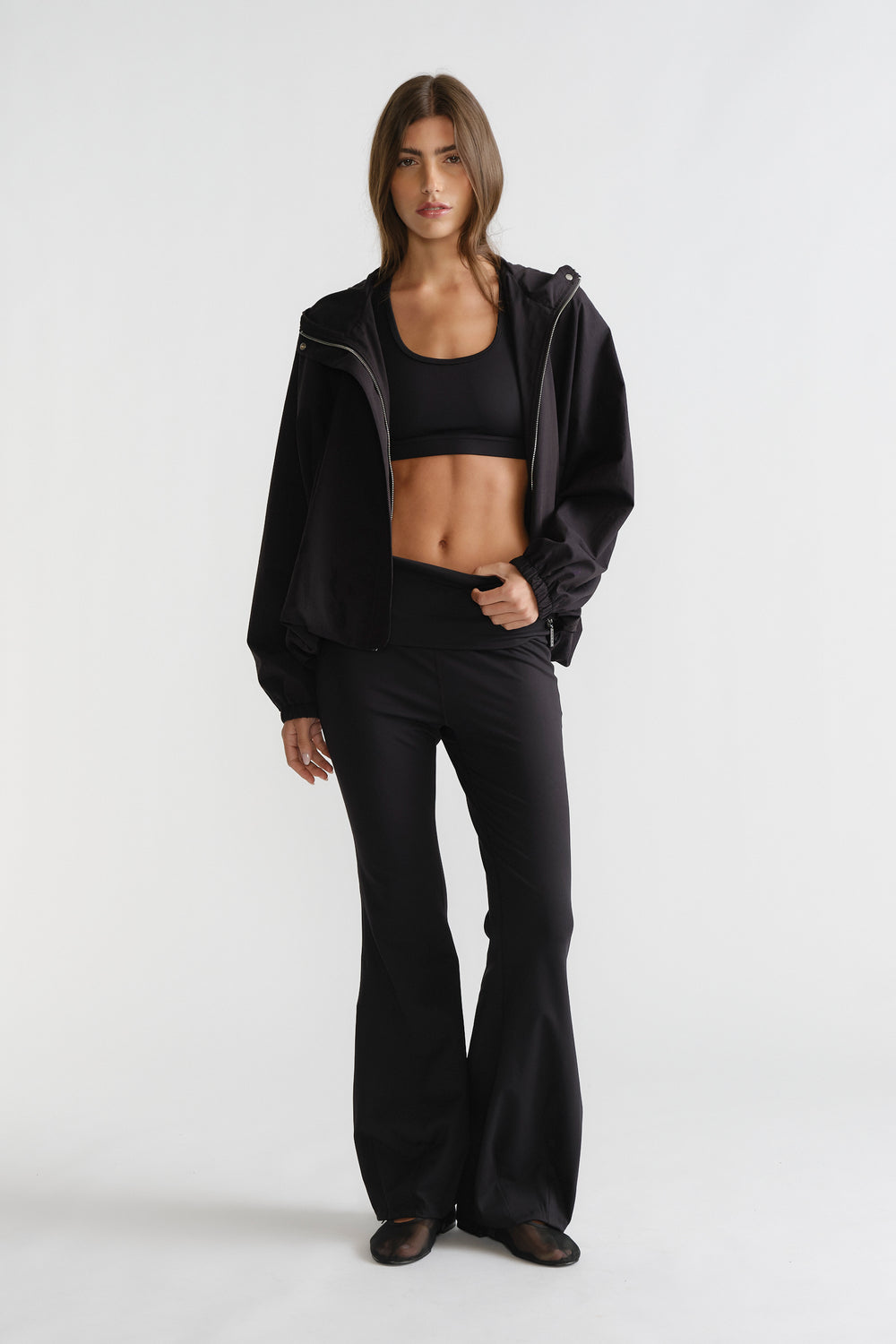 Woman wearing black D-Luxe Flare Legging with a high-rise fit and smooth flare silhouette styled with a sporty black jacket.
