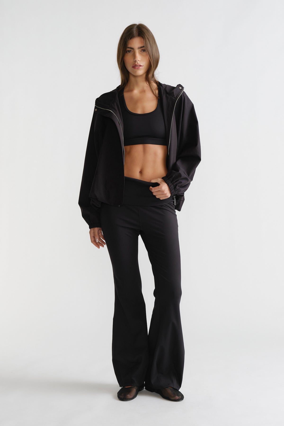 Woman wearing black D-Luxe Flare Legging with a high-rise fit and smooth flare silhouette styled with a sporty black jacket.