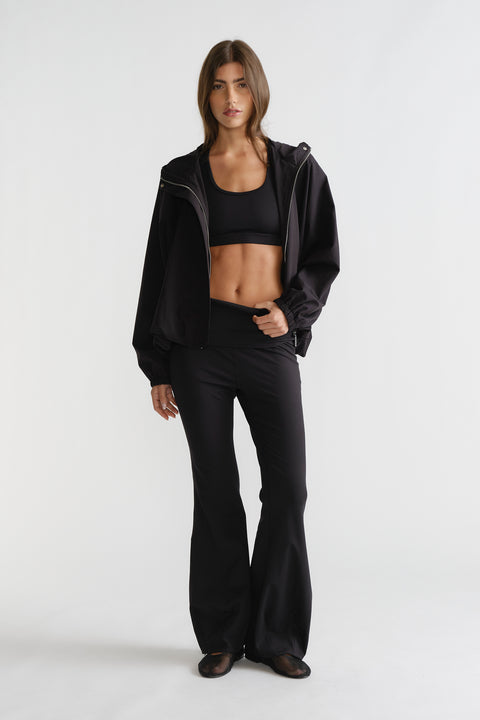 Woman wearing black D-Luxe Flare Legging with a high-rise fit and smooth flare silhouette styled with a sporty black jacket.