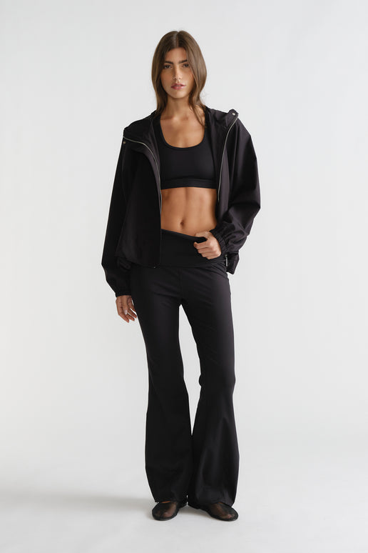 Woman wearing black D-Luxe Flare Legging with a high-rise fit and smooth flare silhouette styled with a sporty black jacket.