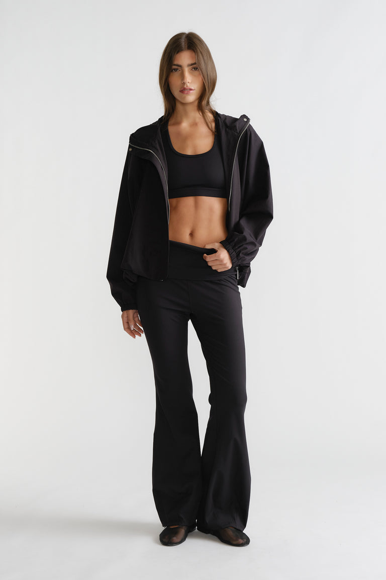 Woman wearing black D-Luxe Flare Legging with a high-rise fit and smooth flare silhouette styled with a sporty black jacket.