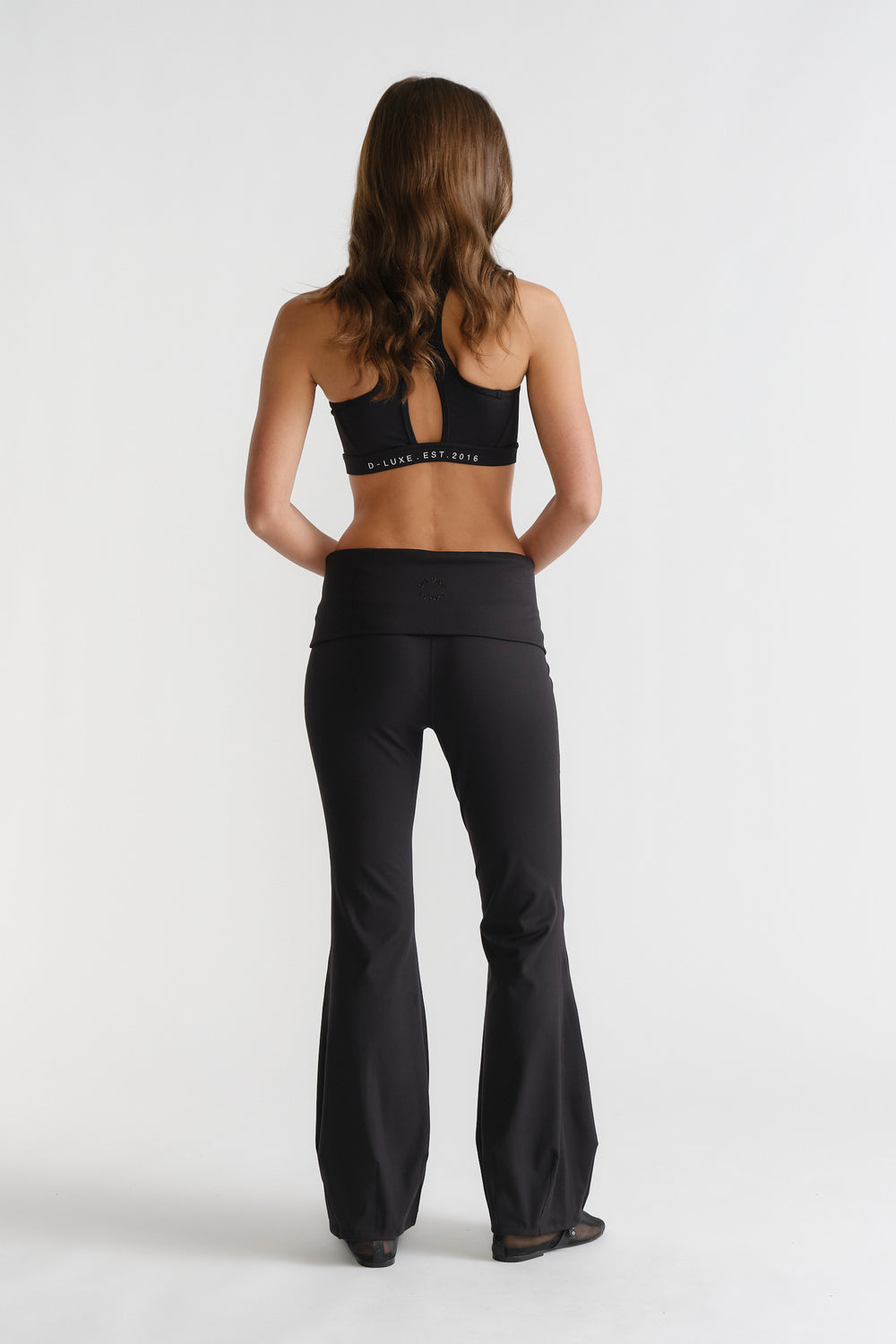 Woman seen from behind wearing black D-Luxe Flare Legging paired with a matching sports bra in a sleek, fitted style.