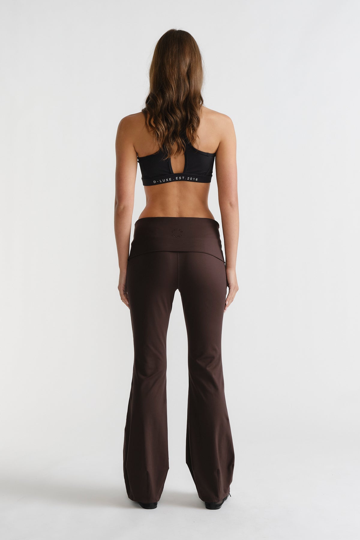 Woman seen from behind wearing cocoa brown D-Luxe Flare Legging with wide waistband, styled with a black sports bra