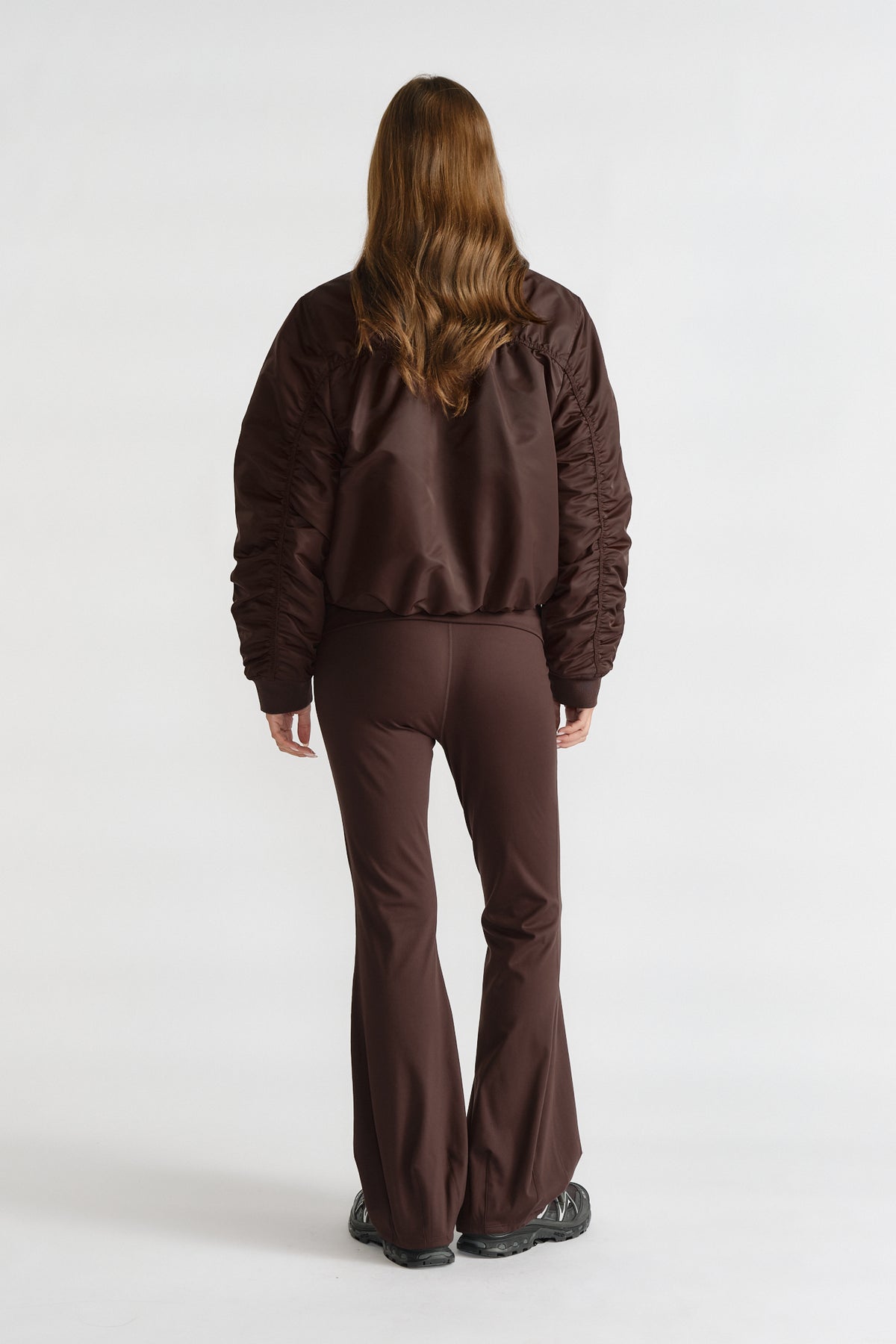 Back view of a model wearing a cocoa brown D-Luxe Collared Bomber Jacket paired with matching flared pants.