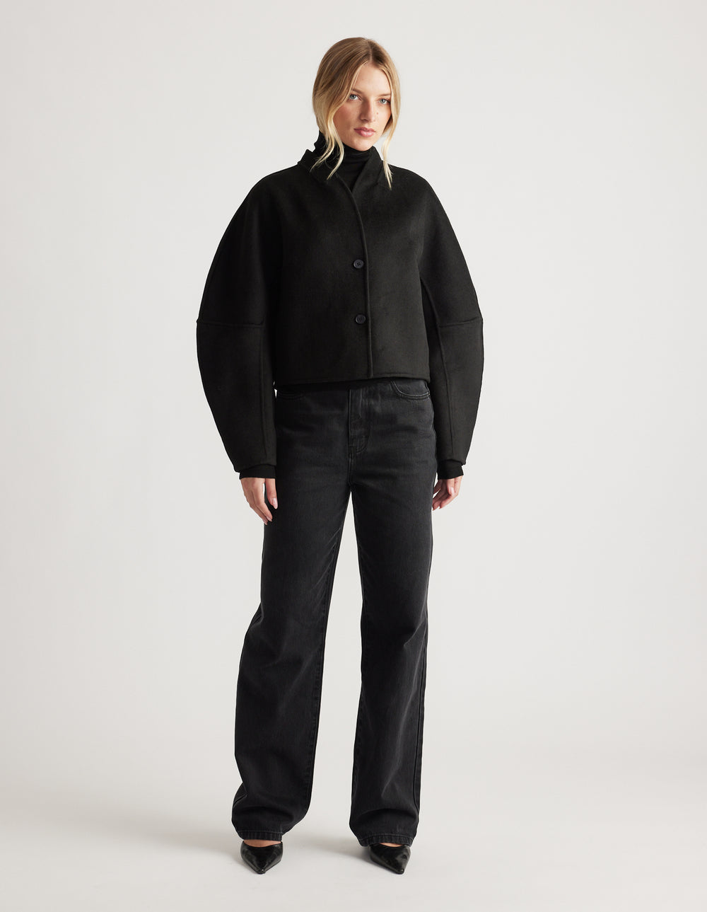 Woman wearing a black cropped jacket with barrel sleeves paired with loose black denim jeans and pointed shoes