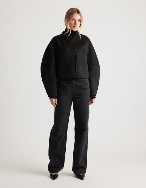 Woman wearing a black cropped jacket with barrel sleeves paired with loose black denim jeans and pointed shoes