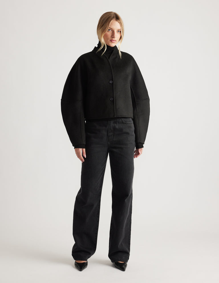 Woman wearing a black cropped jacket with barrel sleeves paired with loose black denim jeans and pointed shoes