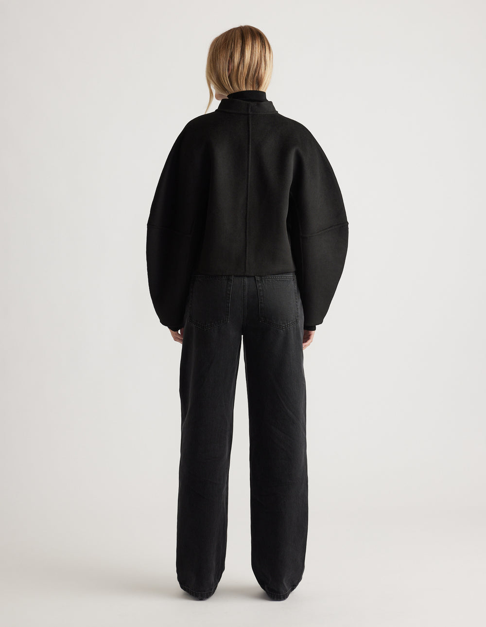 Back view of a woman wearing a black barrel sleeve jacket with relaxed fit high-waisted black jeans