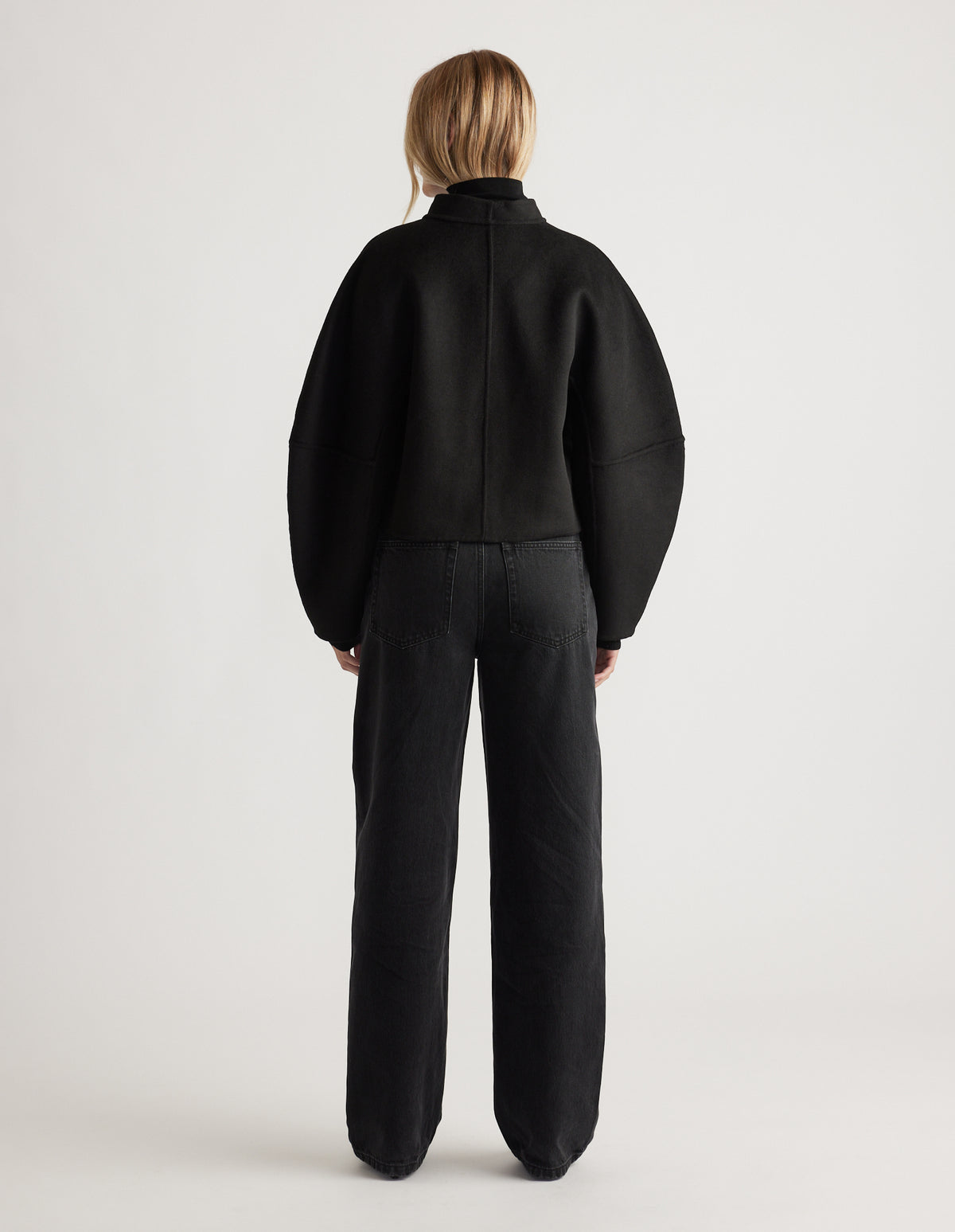 Back view of a woman wearing a black barrel sleeve jacket with relaxed fit high-waisted black jeans