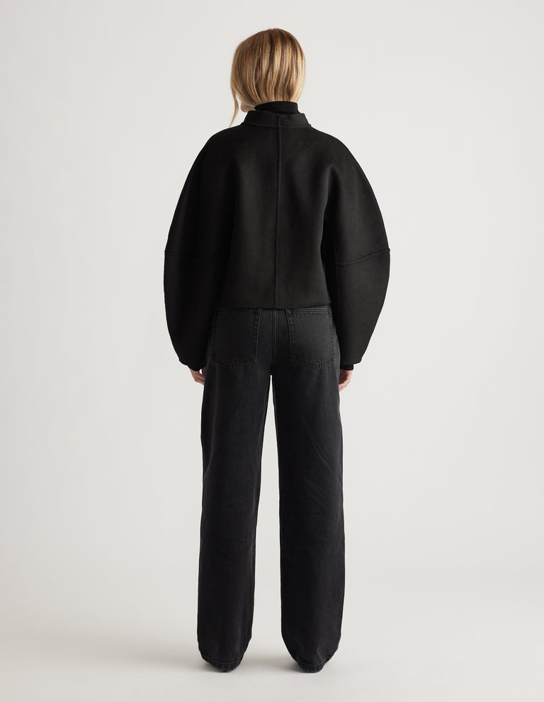 Back view of a woman wearing a black barrel sleeve jacket with relaxed fit high-waisted black jeans