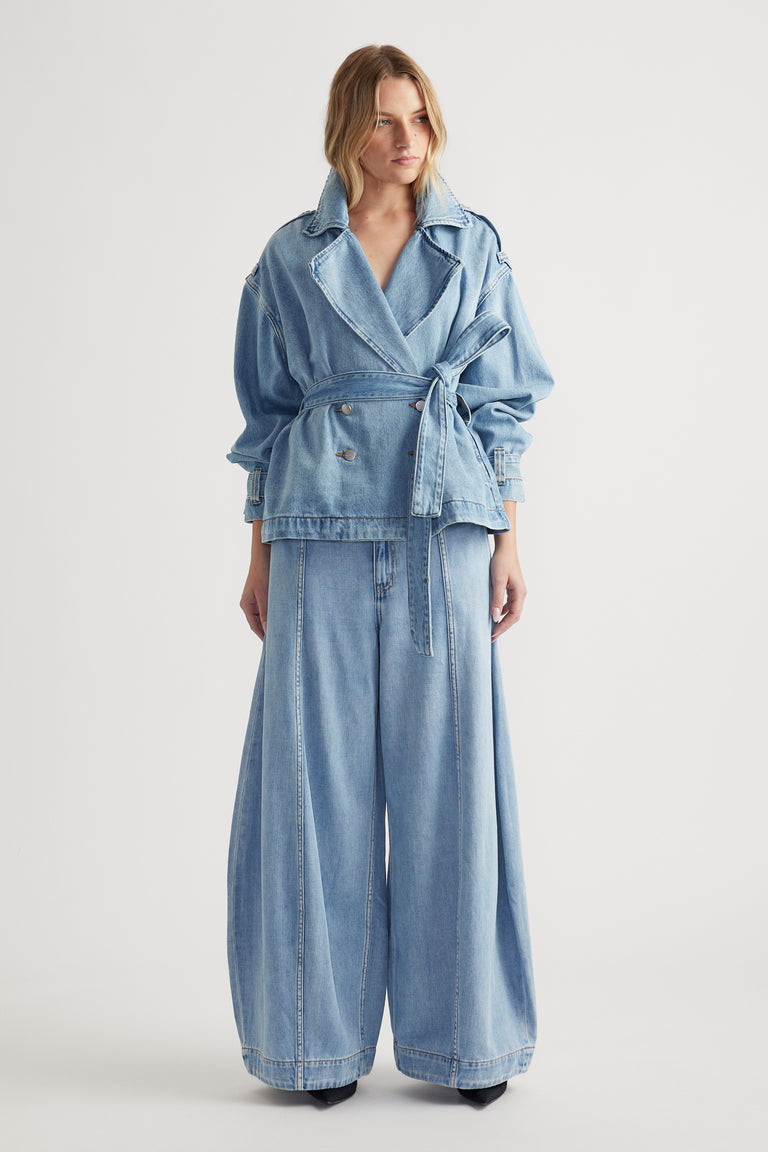 Woman wearing light blue oversized belted denim jacket paired with wide-leg high rise jeans on plain background