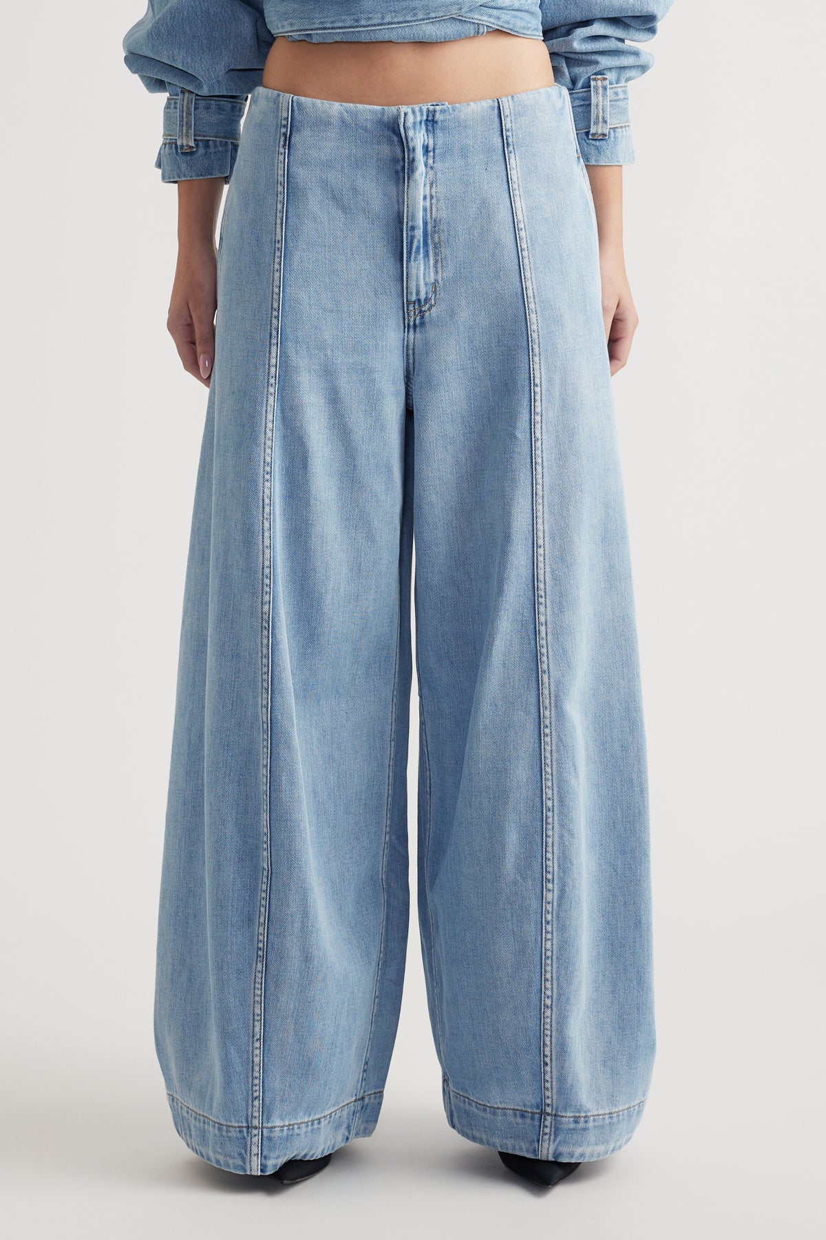 Light wash rigid denim jeans with a high rise waist and voluminous balloon leg silhouette on a plain background