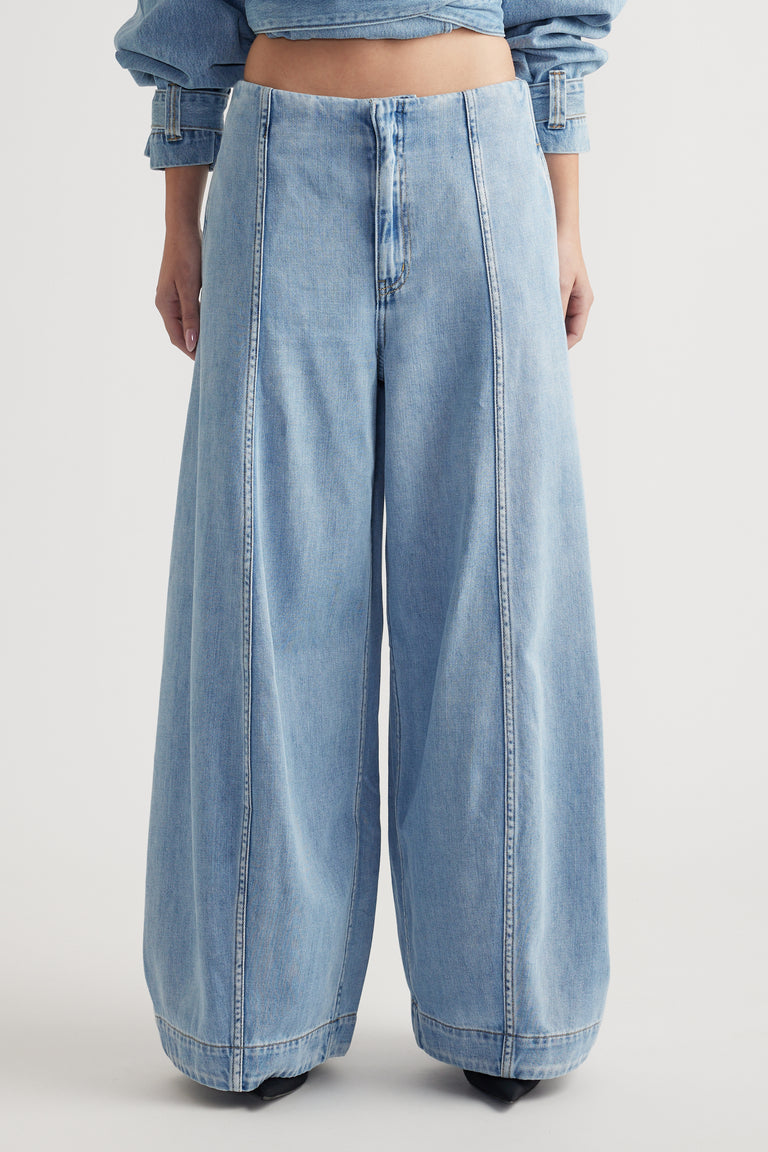 Light wash rigid denim jeans with a high rise waist and voluminous balloon leg silhouette on a plain background