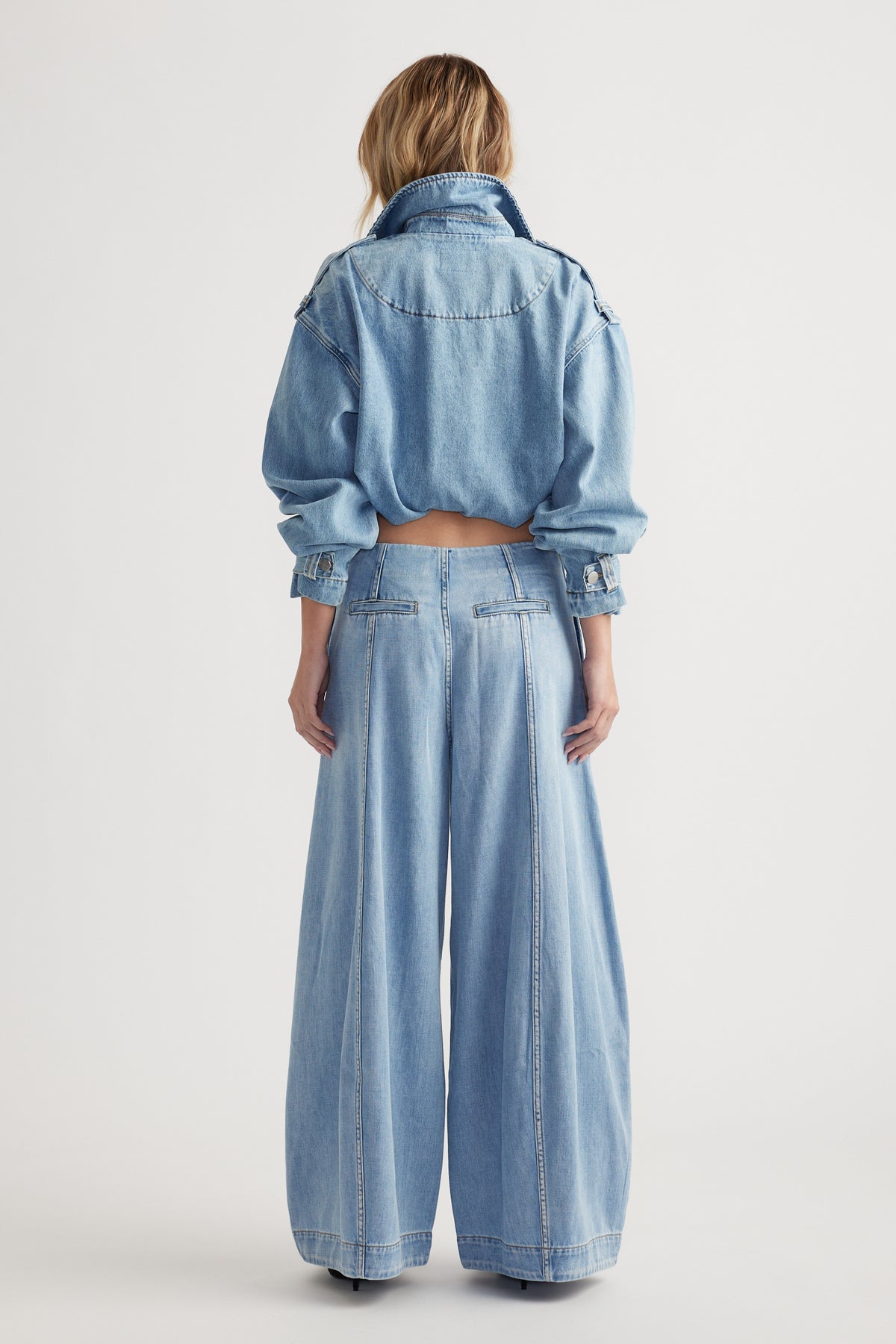 Back view of a woman wearing light blue wide-leg jeans paired with a loose cropped denim jacket